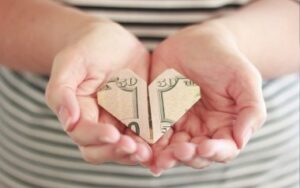 Photo of hands holding heart shaped folded money